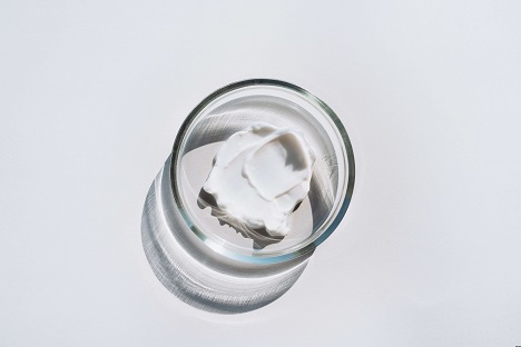 Petri dish with a smear of white cream on gray background.