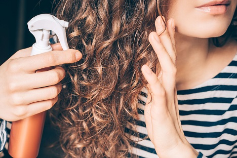 Woman applying spray on curly brown hair